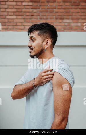 Young bearded Argentinian man showing the patch on his arm after getting vaccinated for COVID-19 Stock Photo