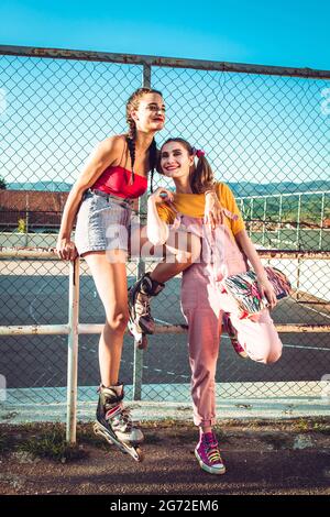 Two teen girls, friends in colorful clothes with roller skates and skate board. Urban style Stock Photo