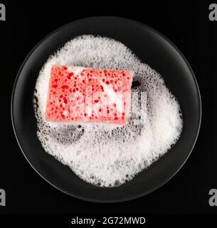 A sponge for washing dishes, with soapy foam, on a black plate, on a black background Stock Photo