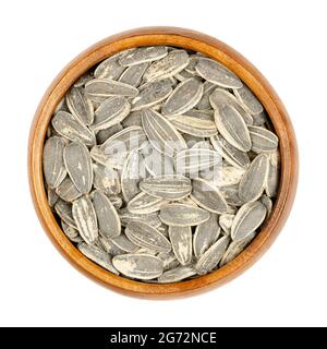 Large sunflower seeds in shells roasted and salted, in a wooden bowl. Whole striped common sunflower seeds, fruits of Helianthus Annuus. Stock Photo