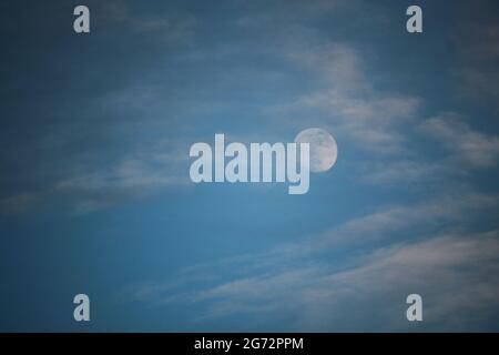 During the day, a beautiful moon rises in the blue sky in the middle of white clouds. Stock Photo