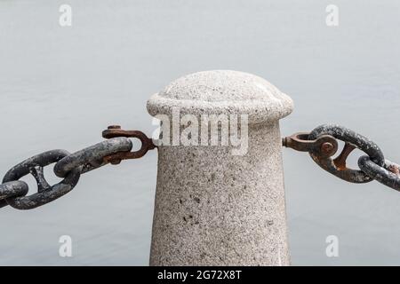 Close up of a beige granite grainy pole connecting rusty black metal chain Stock Photo