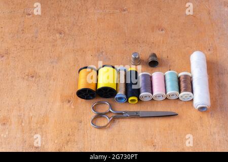 Closeup of colored thread spools, thimbles, and scissors on a wooden background Stock Photo