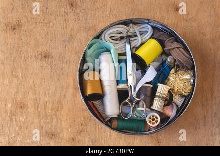Top view of colored thread spools, thimbles, and scissors in a metal box on a wooden background Stock Photo