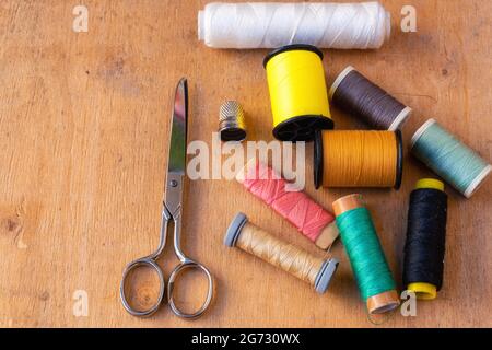 Top view of colored thread spools, thimbles, and scissors on a wooden background Stock Photo