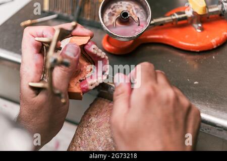 Hands of a dental technician fixing the paste on a dental prosthesis Stock Photo