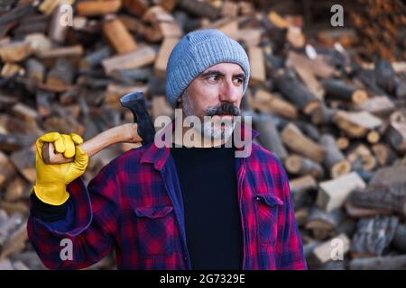 Lumberjack portrait, handsome bearded brunette male model looking seriously with an ax on his shoulder. Stock Photo