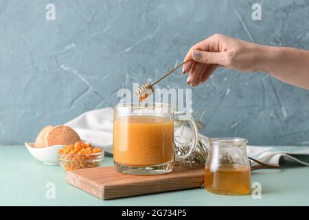 Woman adding honey to healthy sea buckthorn tea in cup Stock Photo