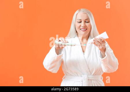Mature woman brushing teeth on color background Stock Photo