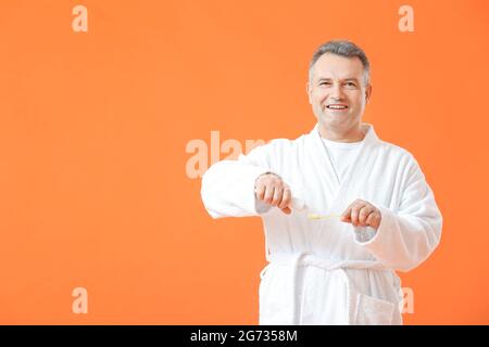 Mature man brushing teeth on color background Stock Photo