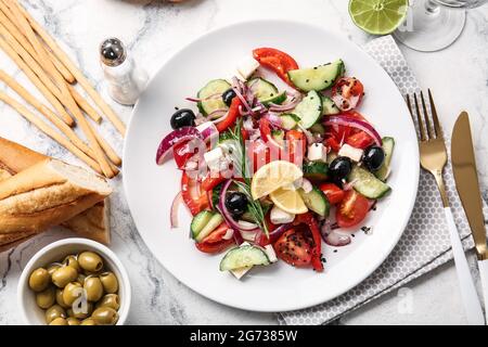 Plate with tasty Greek salad, olives, bread and grissini on light background Stock Photo