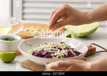 Female chef cooking tasty cabbage salad on table in kitchen, closeup Stock Photo