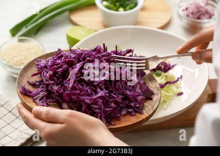 Female chef cooking tasty cabbage salad on table in kitchen, closeup Stock Photo