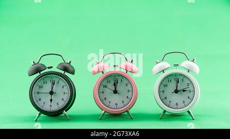 Beautiful three Alarm Clock on green screen Background Alarm Clock Face in daytime Minimal alarm clock Concept Time Zone. Stock Photo