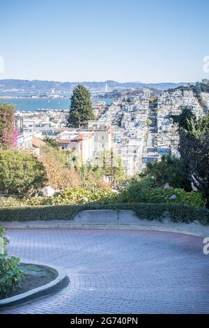 The top of the curved section of Lombard Street (the crookedest street in the world), looking directly down the street and over San Francisco Bay Stock Photo