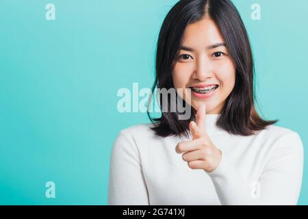 Young beautiful Asian woman smiling point finger at you with a confident expression, Portrait female pointing finger gesture towards you, studio shot