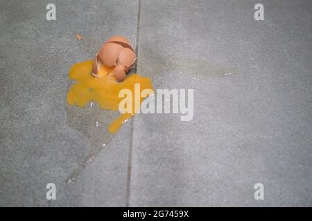 Smashed egg on grey tile floor with cracked and broken shell, egg yolk and albumen splatter Stock Photo