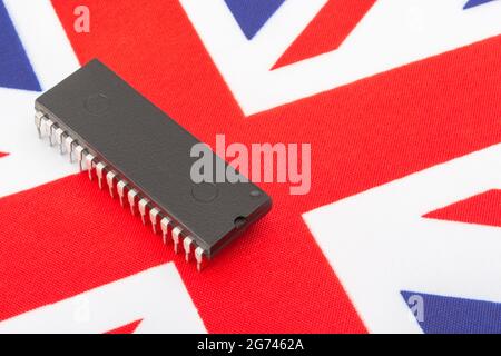 Close shot of integrated circuit / EPROM chip on small UK Union Jack flag. For UK semiconductor shortages, UK chip dependency, UK chip start-ups. Stock Photo