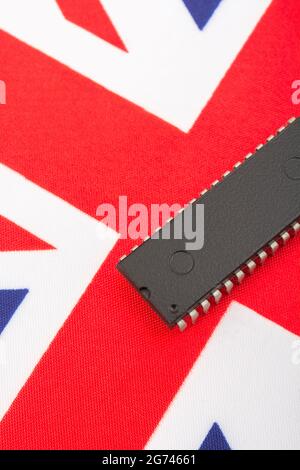 Close shot of integrated circuit / EPROM chip on small UK Union Jack flag. For UK semiconductor shortages, UK chip dependency, UK chip start-ups. Stock Photo