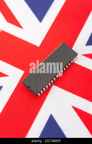 Close shot of integrated circuit / EPROM chip on small UK Union Jack flag. For UK semiconductor shortages, UK chip dependency, UK chip start-ups. Stock Photo