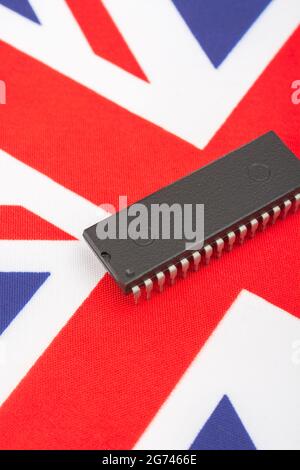 Close shot of integrated circuit / EPROM chip on small UK Union Jack flag. For UK semiconductor shortages, UK chip dependency, UK chip start-ups. Stock Photo