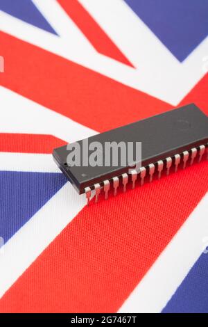 Close shot of integrated circuit / EPROM chip on small UK Union Jack flag. For UK semiconductor shortages, UK chip dependency, UK chip start-ups. Stock Photo