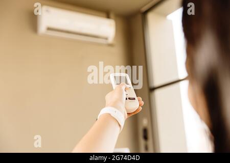 Closeup people using remote control adjust room temperature in home office pointing to Air conditioner in hot summer season. Stock Photo