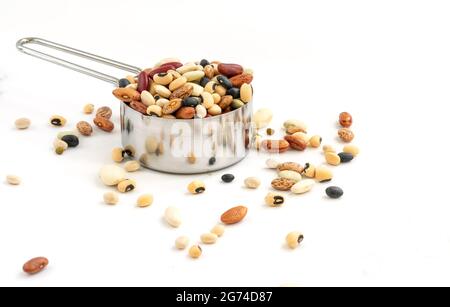 Isolated varieties of beans in stainless steel measuring cup on white background, some beans spread outside. Space for text and design. Stock Photo