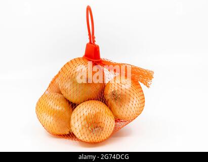 Isolated fresh organic onions in a red net bag on white background. Front view of onion packaging net bag with carrying handle. Stock Photo