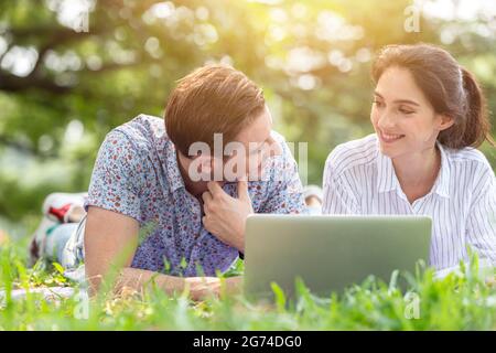 Couple male and women lover using laptop online wireless technology outdoor in the park in holiday vacation together. Stock Photo