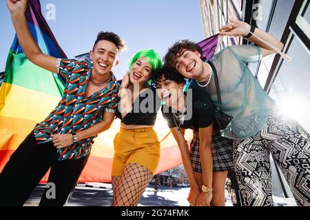 Young LGBTQ+ people celebrating pride together. Group of young queer people smiling cheerfully while holding the rainbow pride flag. Four friends cele Stock Photo