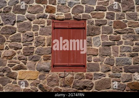 closed red antique window shutters with stone wall surrounding Stock Photo