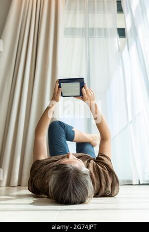 middle aged woman reading electronic book on the floor Stock Photo