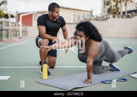 African curvy woman and personal trainer doing pilates workout session outdoor - Main focus on girl face Stock Photo