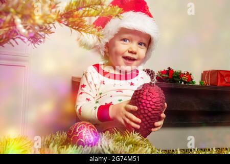 Happy toddler in Sant hat decorate Christmas tree Stock Photo