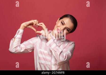 Young beautiful lady making heart shape on pink background Stock Photo