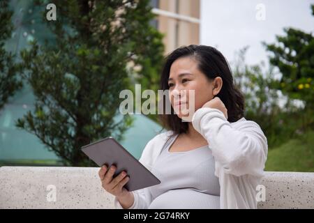A closeup shot of a Southeast-Asian young pregnant woman with a table in a park Stock Photo