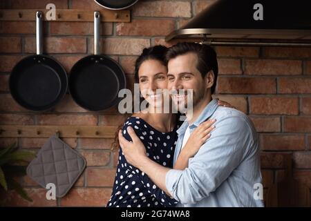 Happy romantic couple hugging at home, smiling, looking away Stock Photo