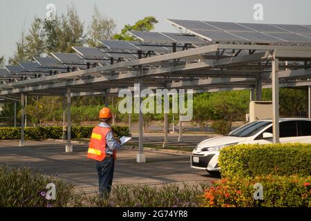 Asian engineers inspecting solar panels mounted on roofs of car parks which is the most efficient use due to limited space. Stock Photo