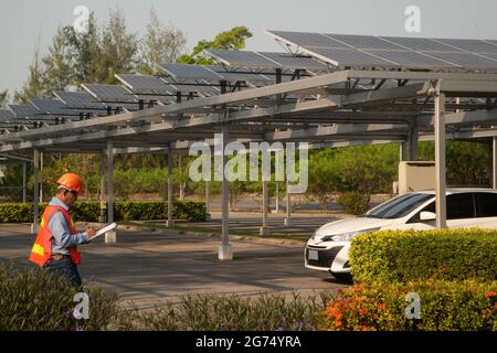 Asian engineers inspecting solar panels mounted on roofs of car parks which is the most efficient use due to limited space. Stock Photo