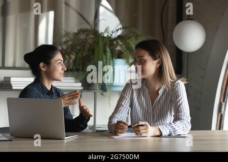 Diverse female office employees discussing project, talking at meeting table Stock Photo