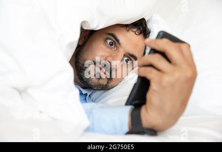 middle agem man in bed looking at his phone, social media addiction Stock Photo