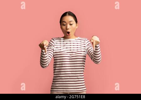 Amazing Offer. Shocked Asian Female Pointing Down With Two Fingers Stock Photo