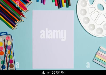 Art supplies for school painting and a blank sheet of paper on a blue background with copy space for text. Colorful pencils, markers, paints and child Stock Photo