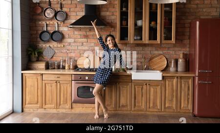 Excited barefooted millennial woman dancing to music in loft kitchen Stock Photo