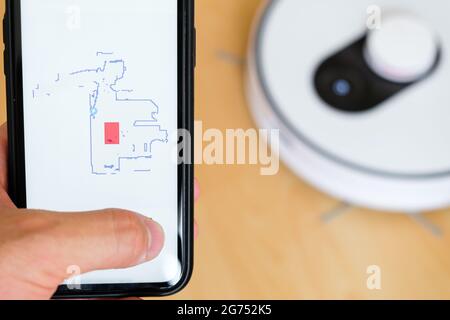 Close up a mobile phone application for managing of robot vacuum cleaner in mans hand. Smart technology for housekeeping  Stock Photo