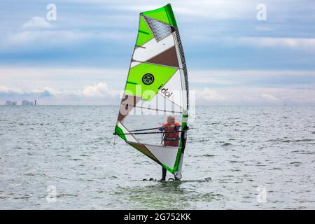 Christchurch, Dorset UK. 11th July 2021. UK weather: cloudy and warm at Steamers Point, Christchurch, as wind surfers take to the sea with the Needles, Isle of Wight in the distance. Mature woman adult windsurfing wind surfing windsurfers windsurfer wind surfers wind surfer. Credit: Carolyn Jenkins/Alamy Live News Stock Photo