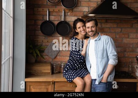 Happy young married couple hugging in kitchen, looking at camera Stock Photo