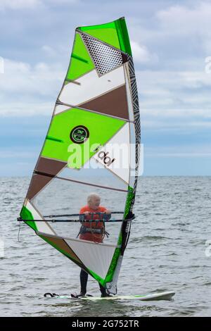 Christchurch, Dorset UK. 11th July 2021. UK weather: cloudy and warm at Steamers Point, Christchurch, as wind surfers take to the sea. Mature woman adult windsurfing wind surfing windsurfers windsurfer wind surfers wind surfer. Credit: Carolyn Jenkins/Alamy Live News Stock Photo