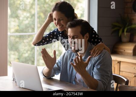 Overjoyed millennial couple using laptop, looking at screen Stock Photo